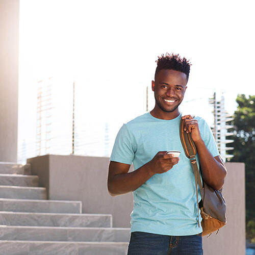 Man wearing a light blue shirt with a backpack over one shoulder and holding a cell phone