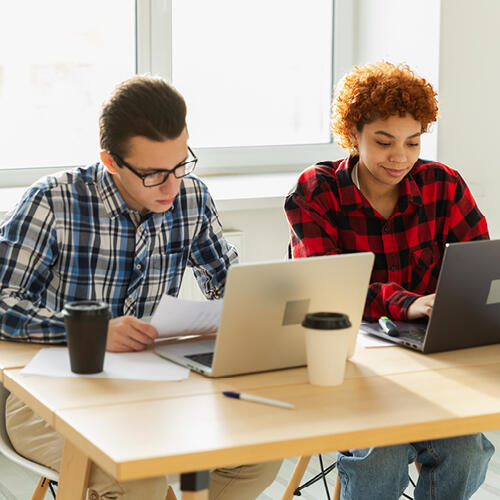 Two students sitting at a table with laptops