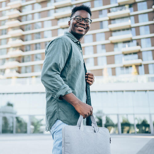 Man in glasses smiling, holding a laptop bag