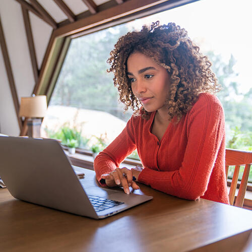 A law student in a red shirt sitting at a table studying for the bar exam on a laptop.