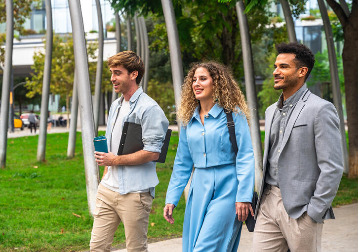 Three smiling diverse young lawyers walking and talking in a city park.