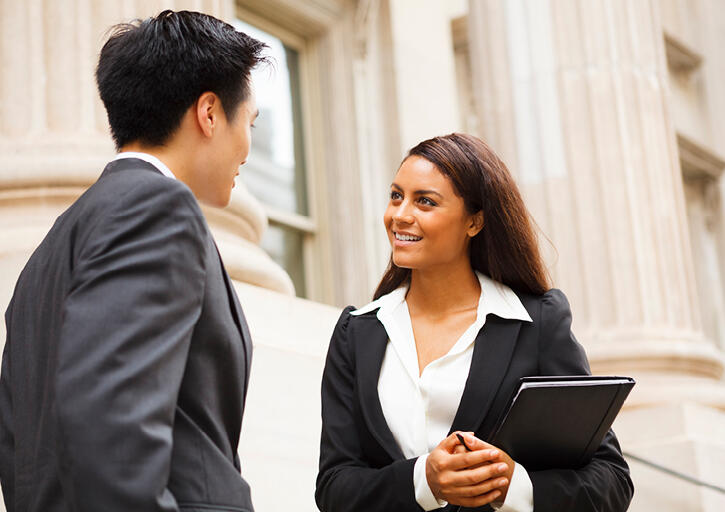 Professional woman and man having a discussion on the stairs of a stately building. The woman is holding a notebook.