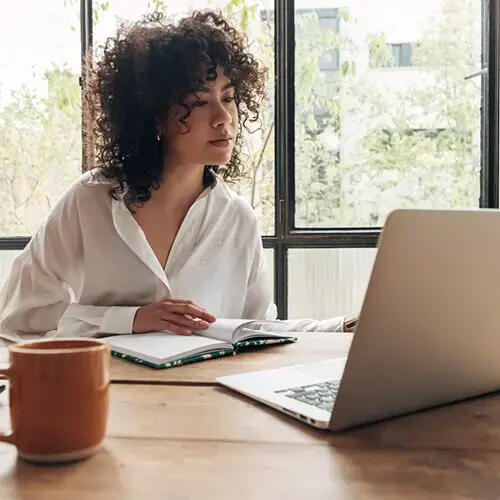 Woman studying for the bar exam with Helix Bar Review at home with laptop, taking notes in notebook. 