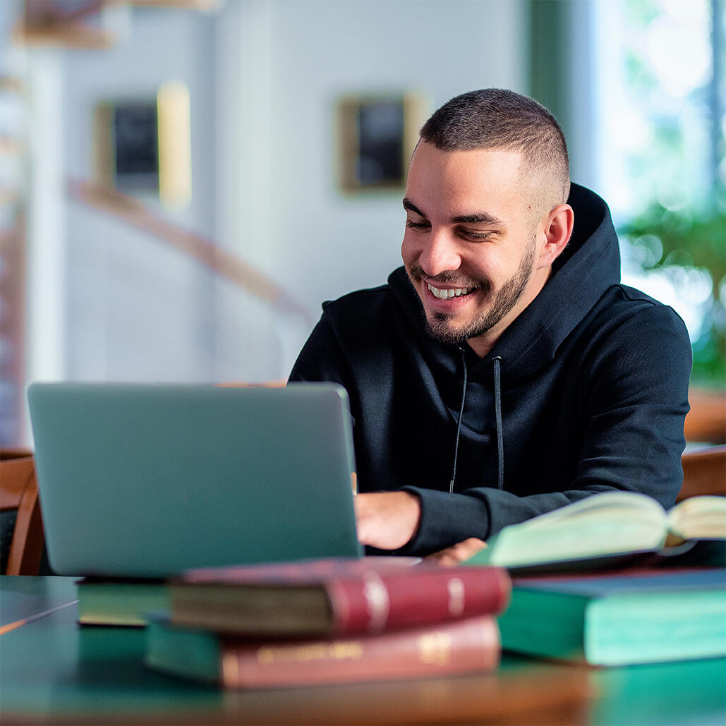 Male student using notebook and books and learning in the university library