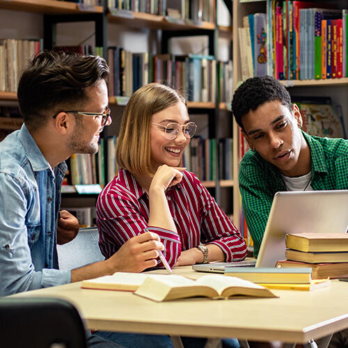 Three students in the in a library looking at a laptop screen