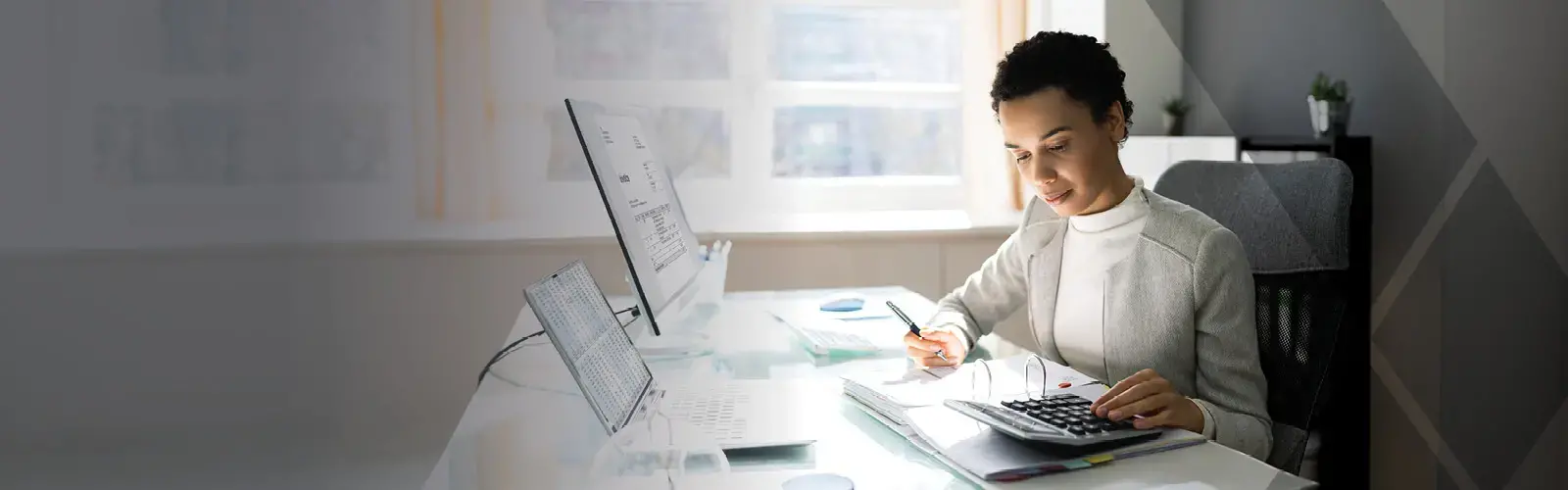 Young professional sitting at a desk and looking down at a calculator with pen in hand.