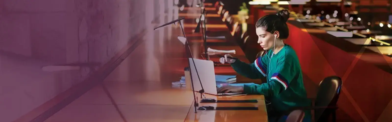 Student sitting at a library table, looking at a laptop 