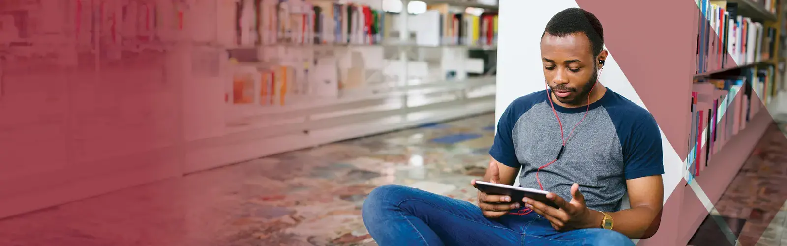A student sits in library on tablet with earphones in 