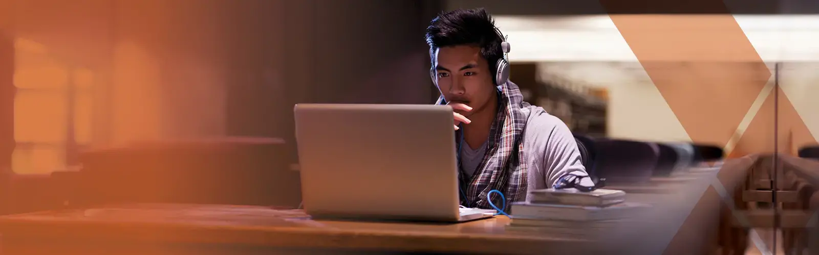 Student in the library with headphones looking at laptop 