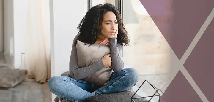 Pensive young adult looking outside on windowsill at home alone 