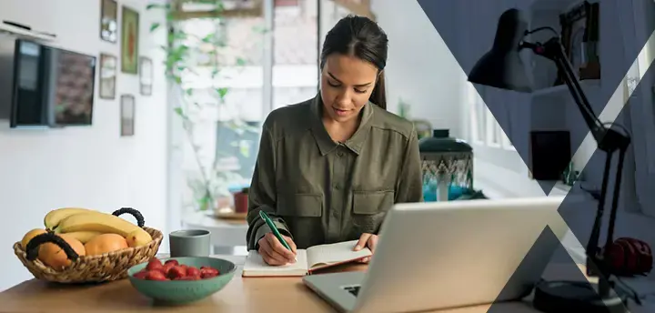Young adult sitting at desk taking notes in notebook 